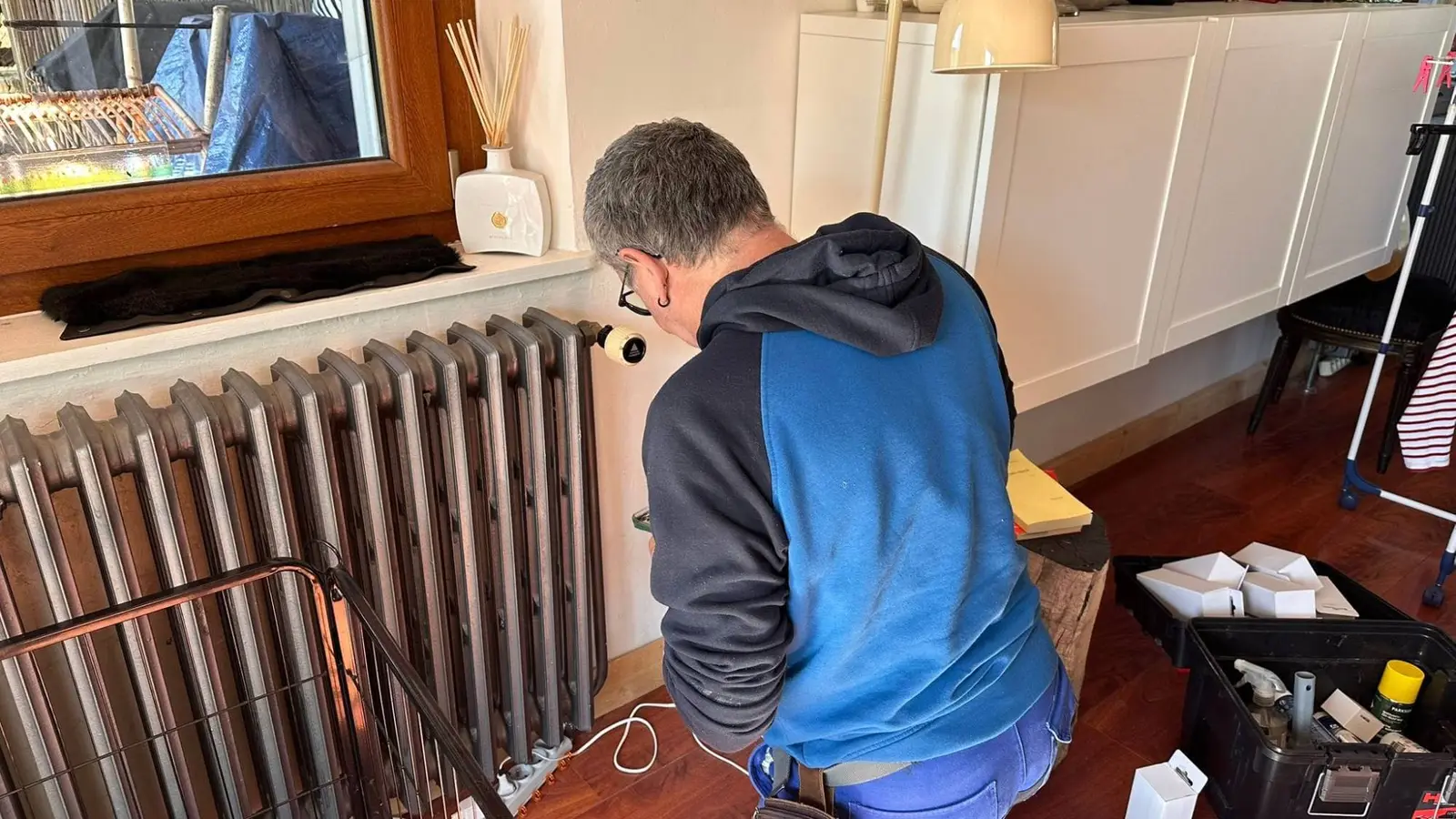 Technicien installant une tête thermostatique connectée sur un radiateur, dans un logement occupé