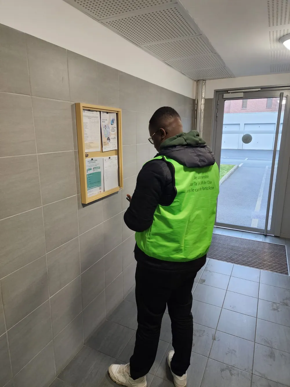 Contrôleur QSBAIL en gilet identifié vérifiant l'affichage réglementaire dans le hall d'une résidence